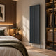 Reina Neva vertical single-panel designer radiator in anthracite, fitted in a bedroom