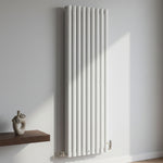 White vertical radiator on a light gray wall with a wooden shelf and decorative vase.